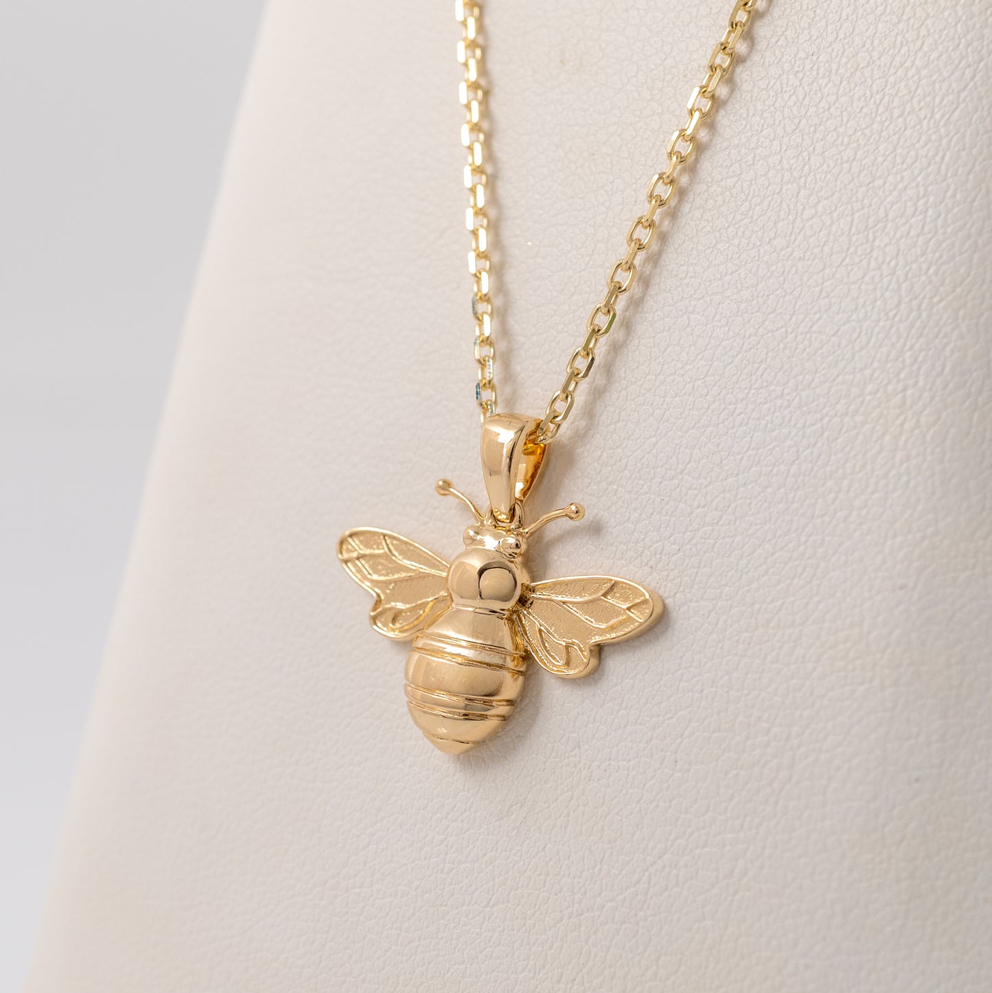 9ct gold bee pendant necklace displayed against a jewellery cushion, highlighting its polished gold finish and intricate wing details