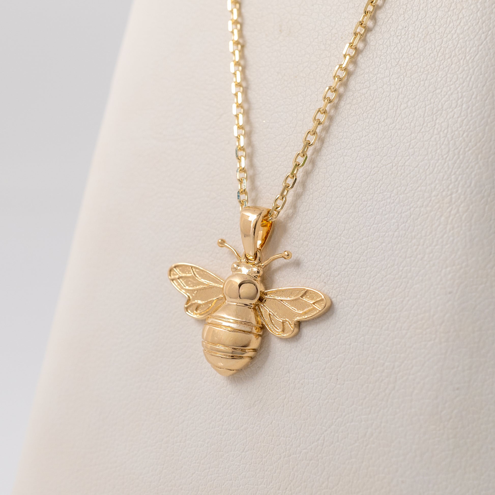 9ct gold bee pendant necklace displayed against a jewellery cushion, highlighting its polished gold finish and intricate wing details