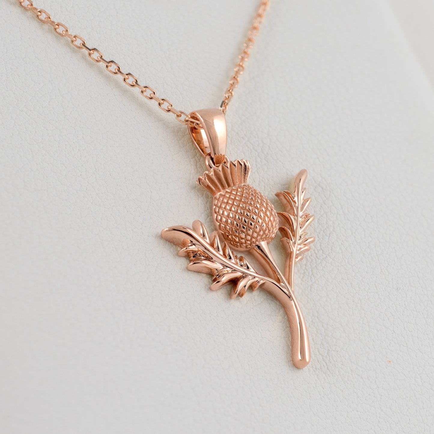 Rose gold thistle pendant necklace on a light gray background