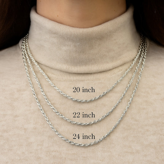 Three silver chains of different lengths worn on a person's neck against a beige background.