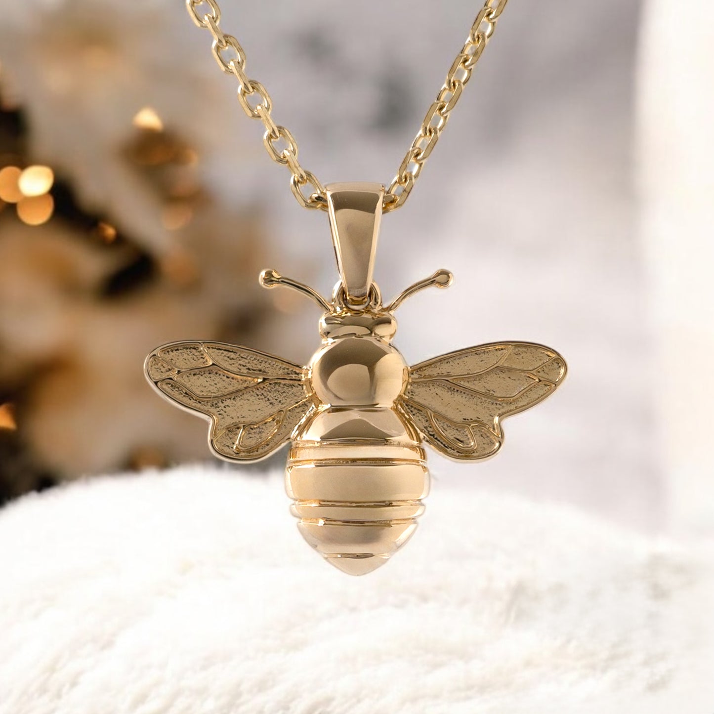 9ct gold bee pendant necklace by Hunters Fine Jewellery, displayed on a soft cream cushion with warm lighting