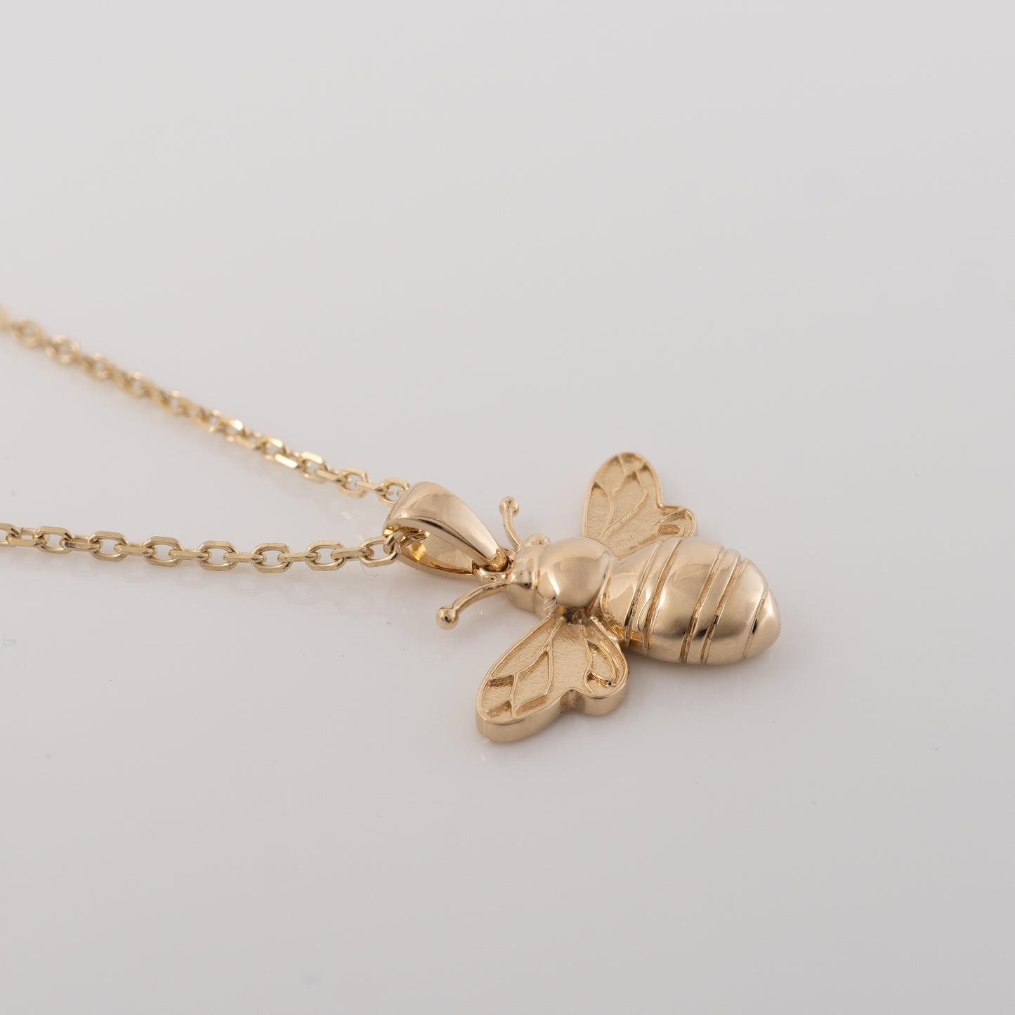 Side view of 9ct gold bee pendant showcasing smooth polished body and delicate curved antennae
