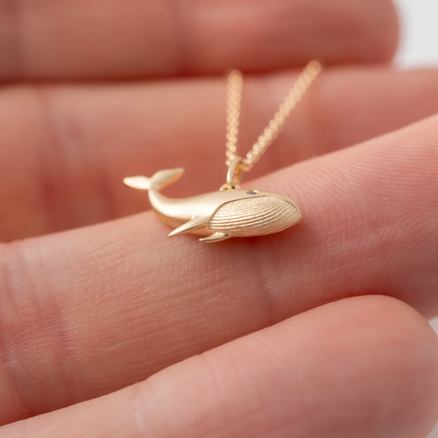 9ct Matte gold whale pendant in a hand to show scale