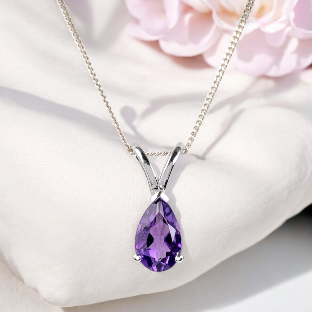 amethyst teardrop necklace in silver displayed on white pillow with pink flower