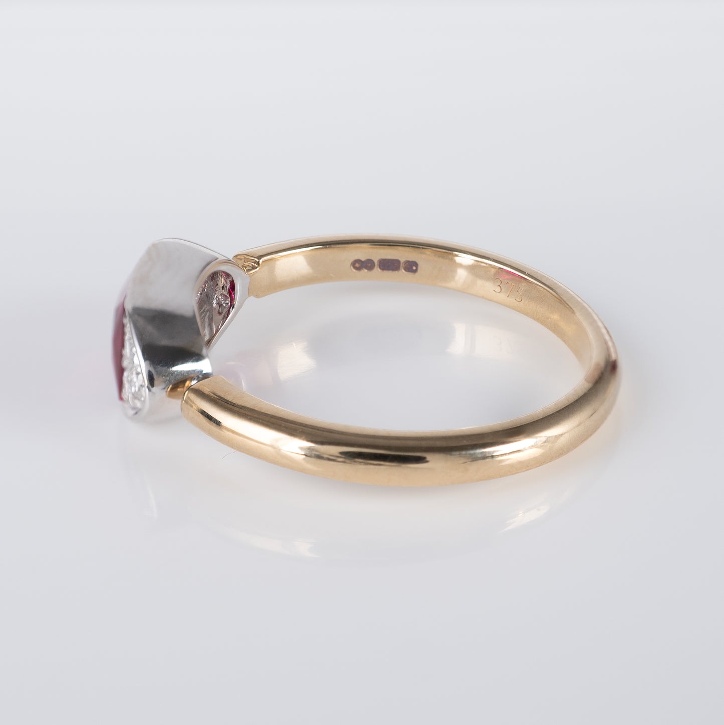 Contemporary ruby ring in 9ct gold, side view showing hallmarks and radiant-cut lab ruby with diamond accents by Hunters Fine Jewellery.