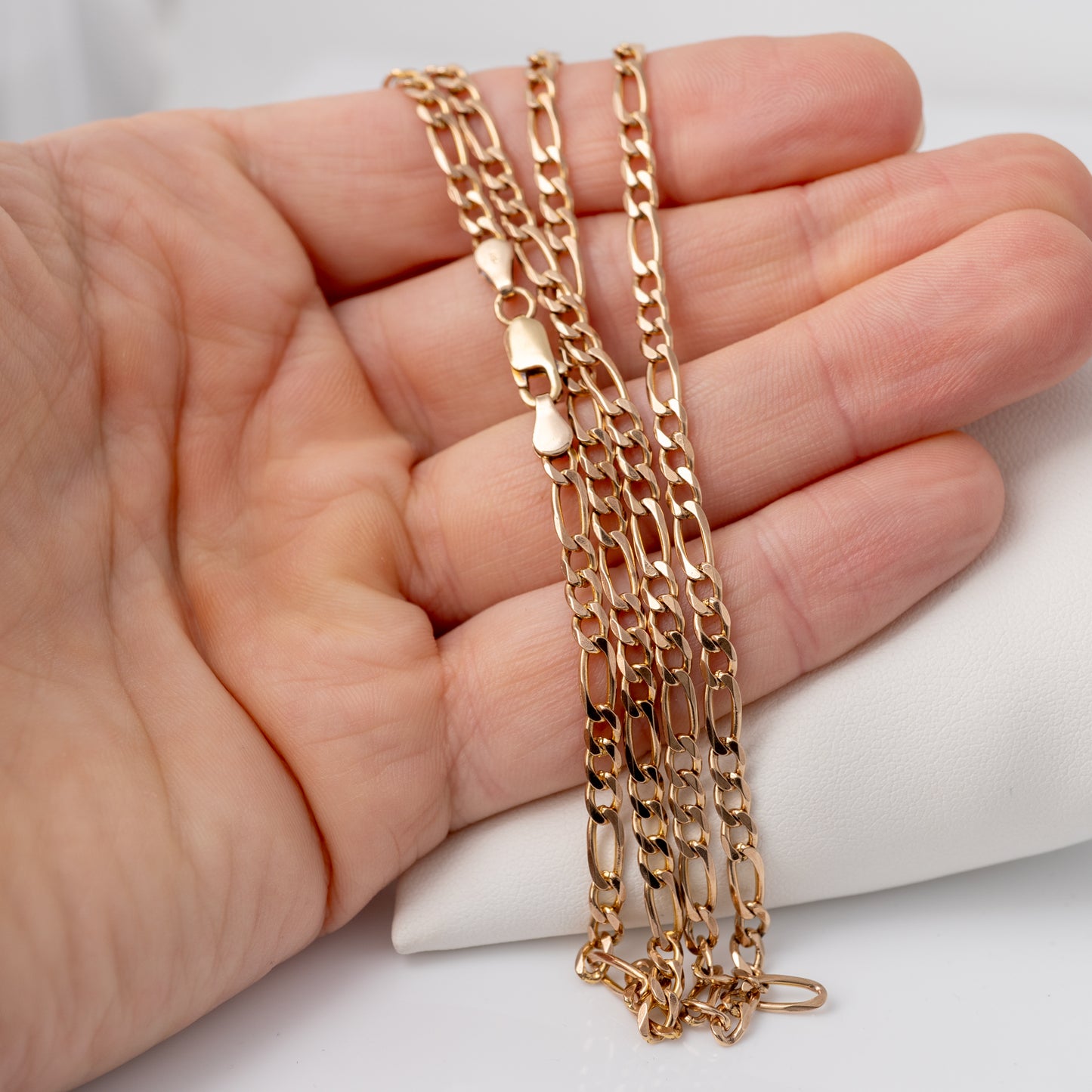 Hand holding the gold Figaro chain to show its size and scale