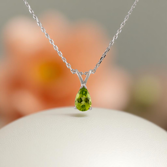peridot necklace silver teardrop pendant hanging in front of a peach background