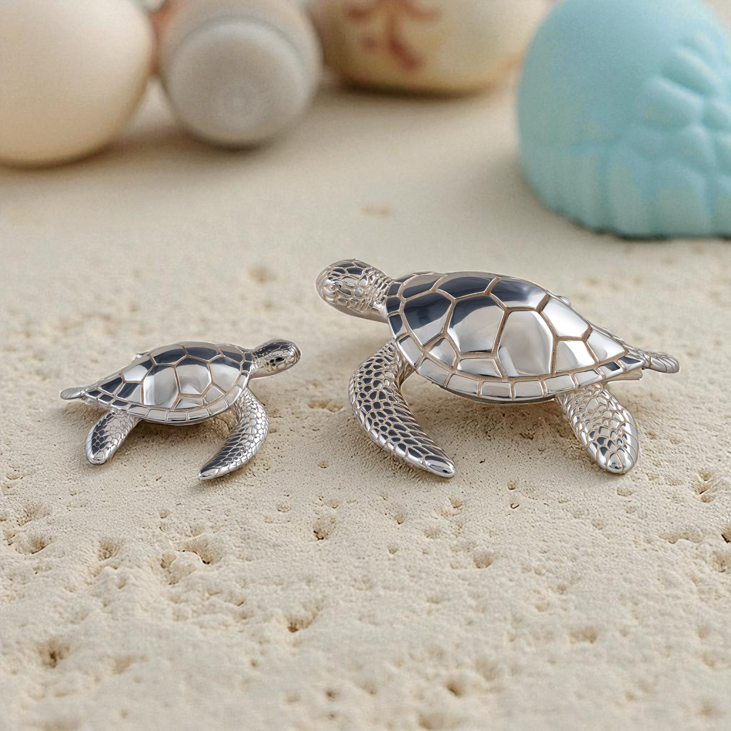 Small and large sterling silver sea turtle figurines displayed on sandy surface with seashells