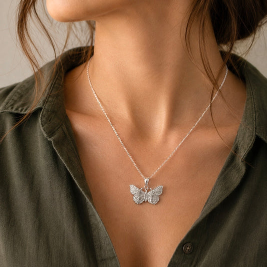 A close-up of a model wearing a delicate silver butterfly pendant necklace on a fine chain, styled with an olive green shirt.