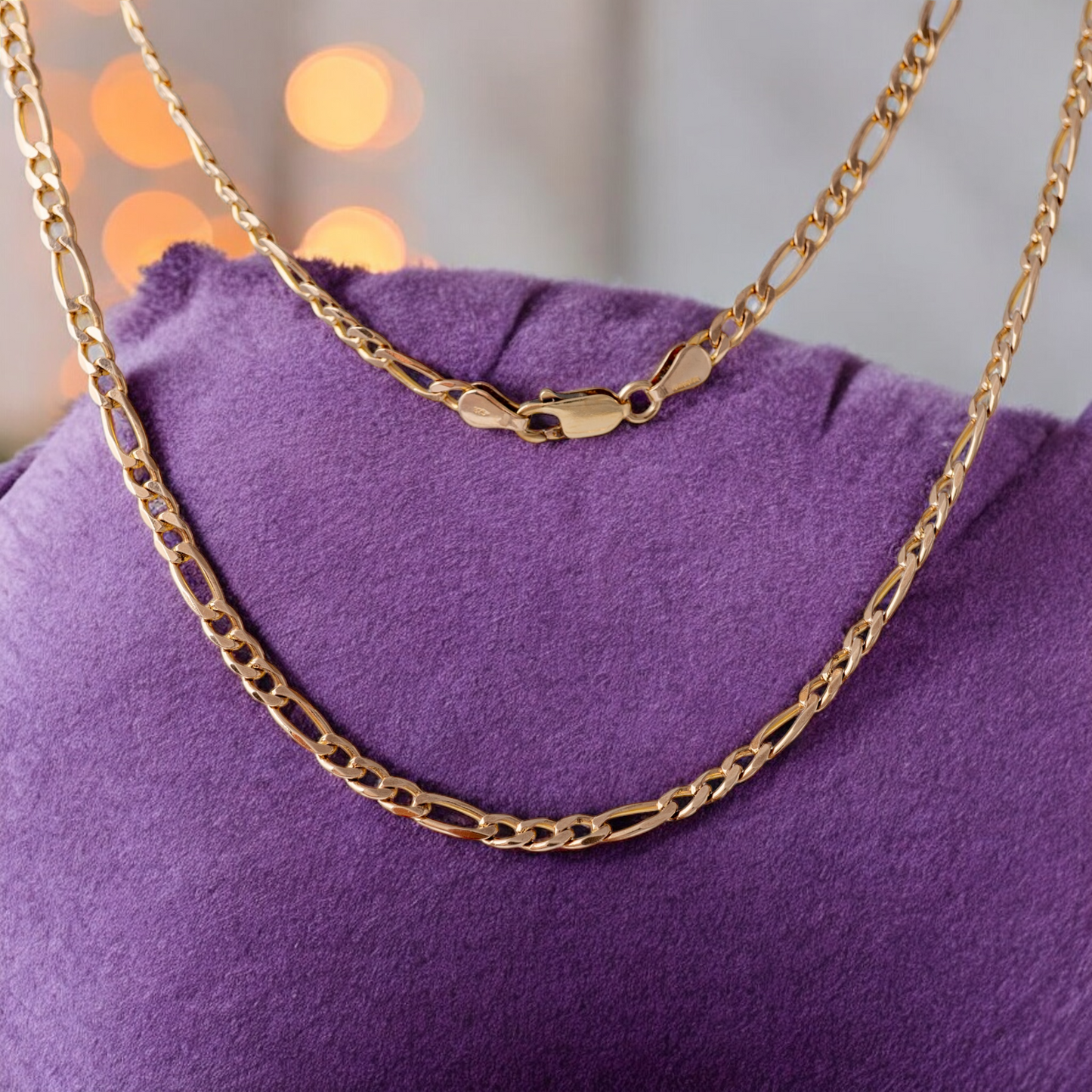 Women’s gold Figaro chain necklace, draped over a purple cushion