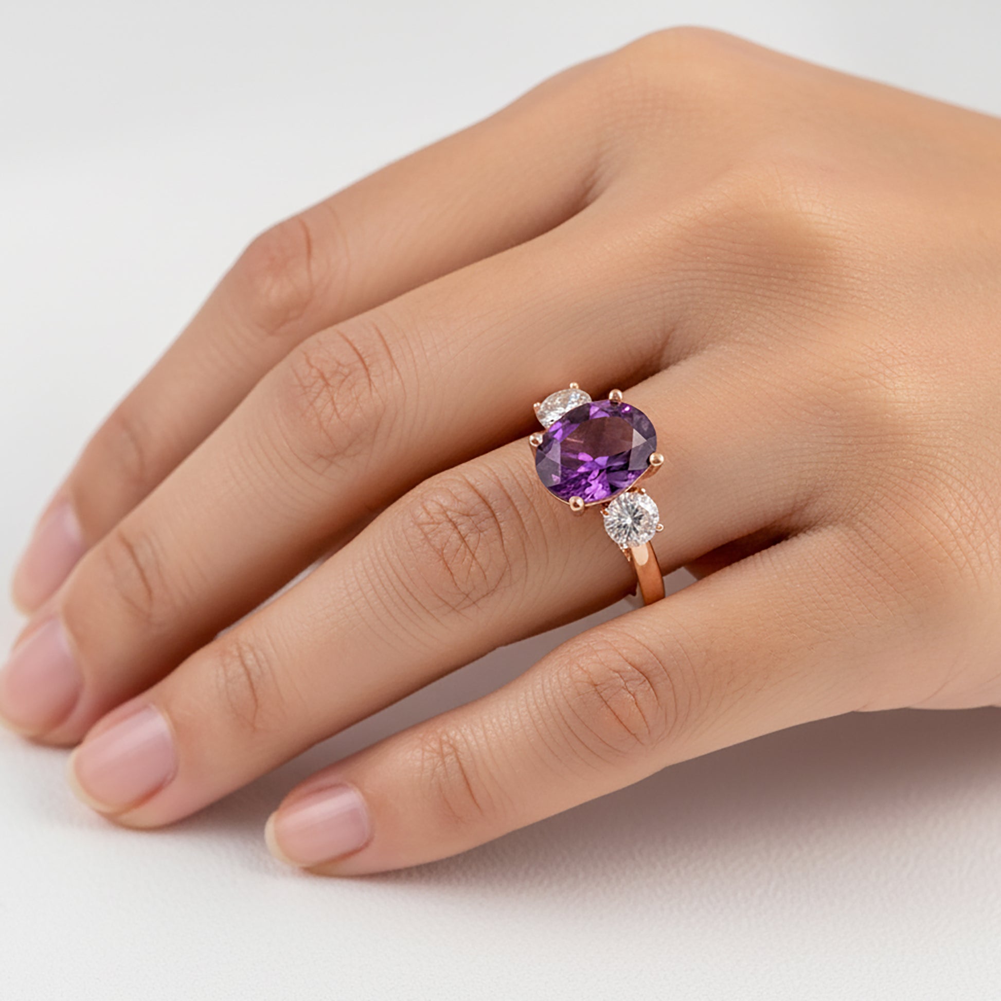 Hand wearing a ring with a purple gemstone on a light background