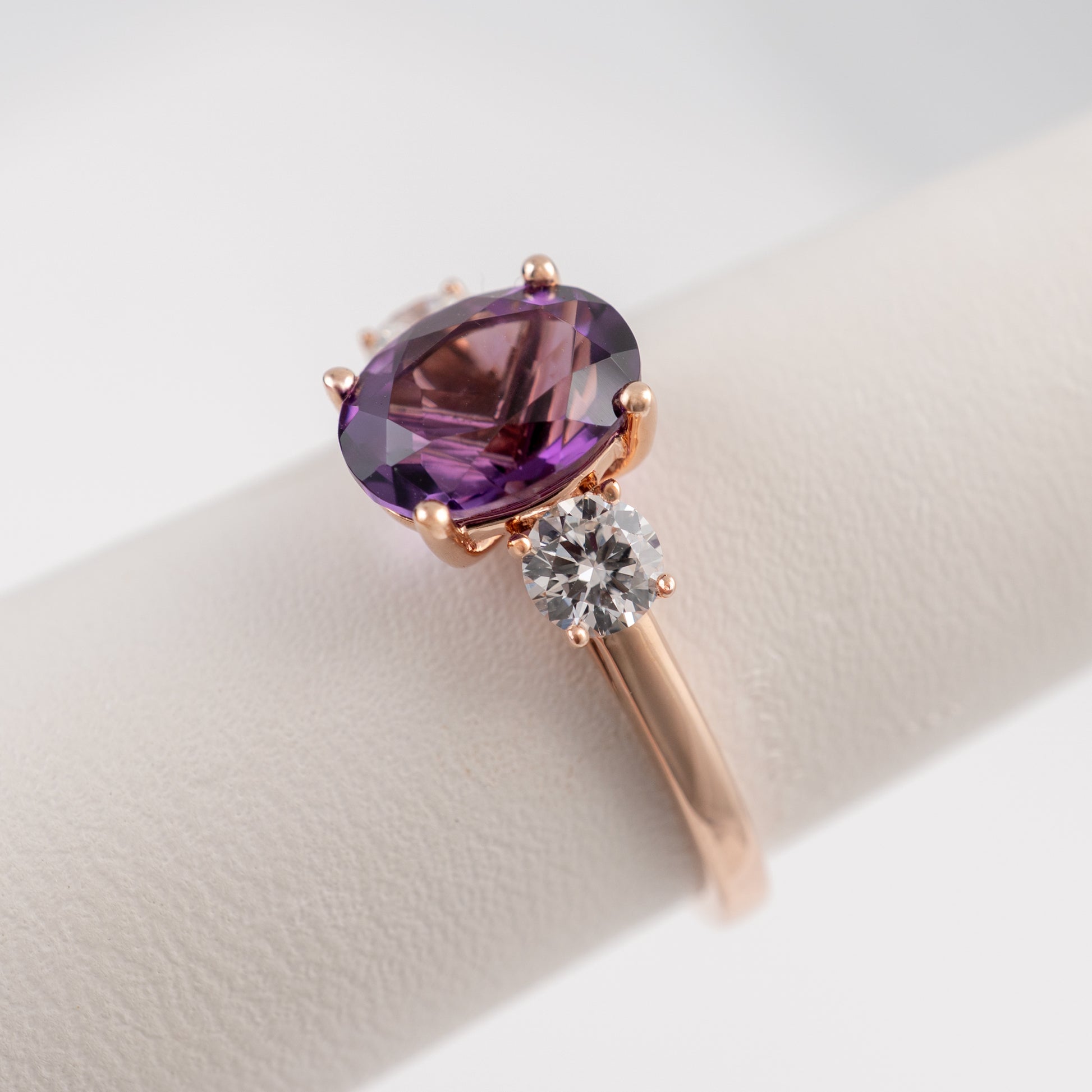 Rose gold amethyst three stone ring on display stand – angled view