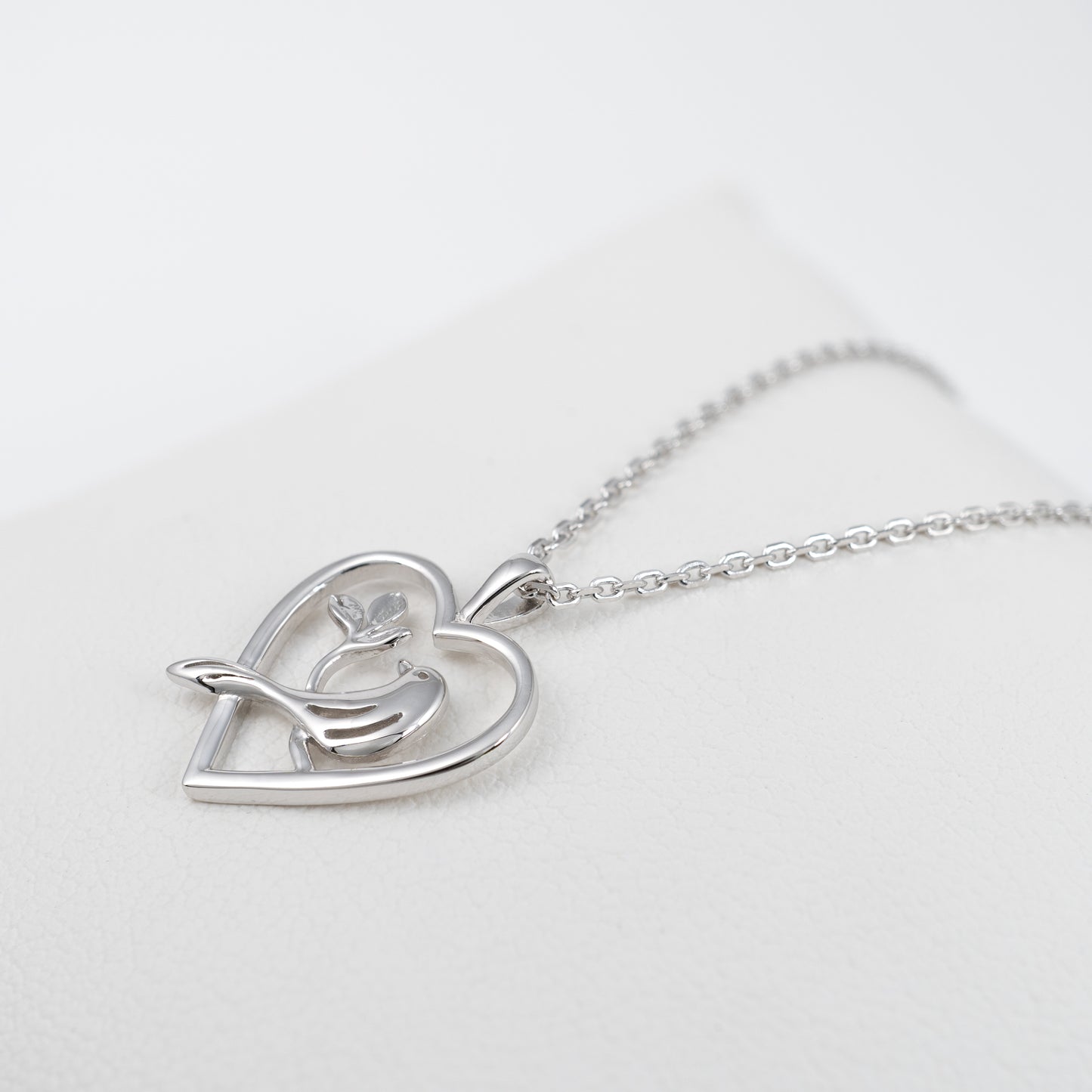 Sterling silver bird heart necklace laid flat at an angle