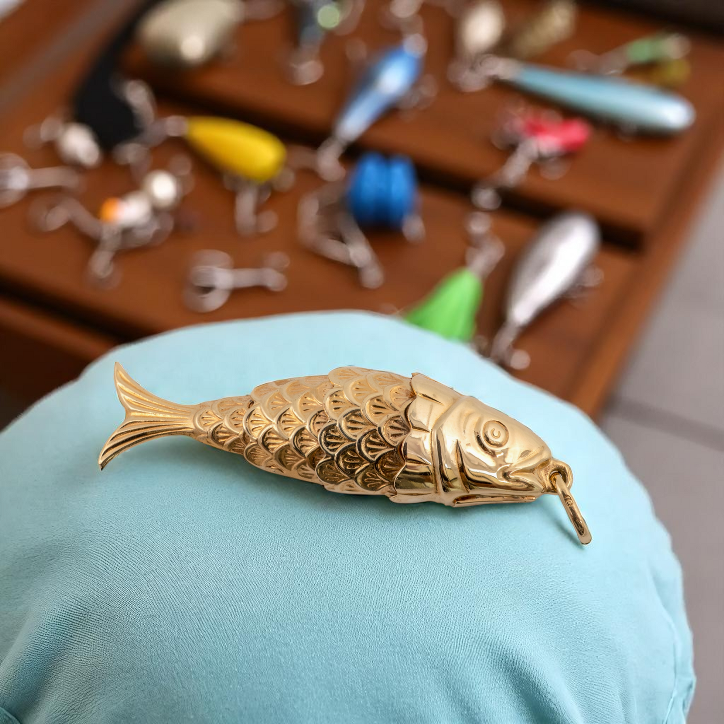 Articulated gold fish pendant resting on blue cloth with fishing tackle theme background