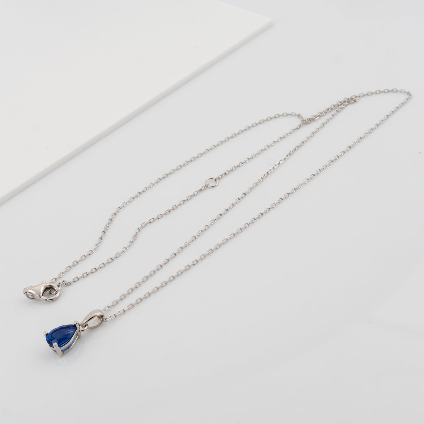 Blue sapphire teardrop pendant with silver chain laid flat