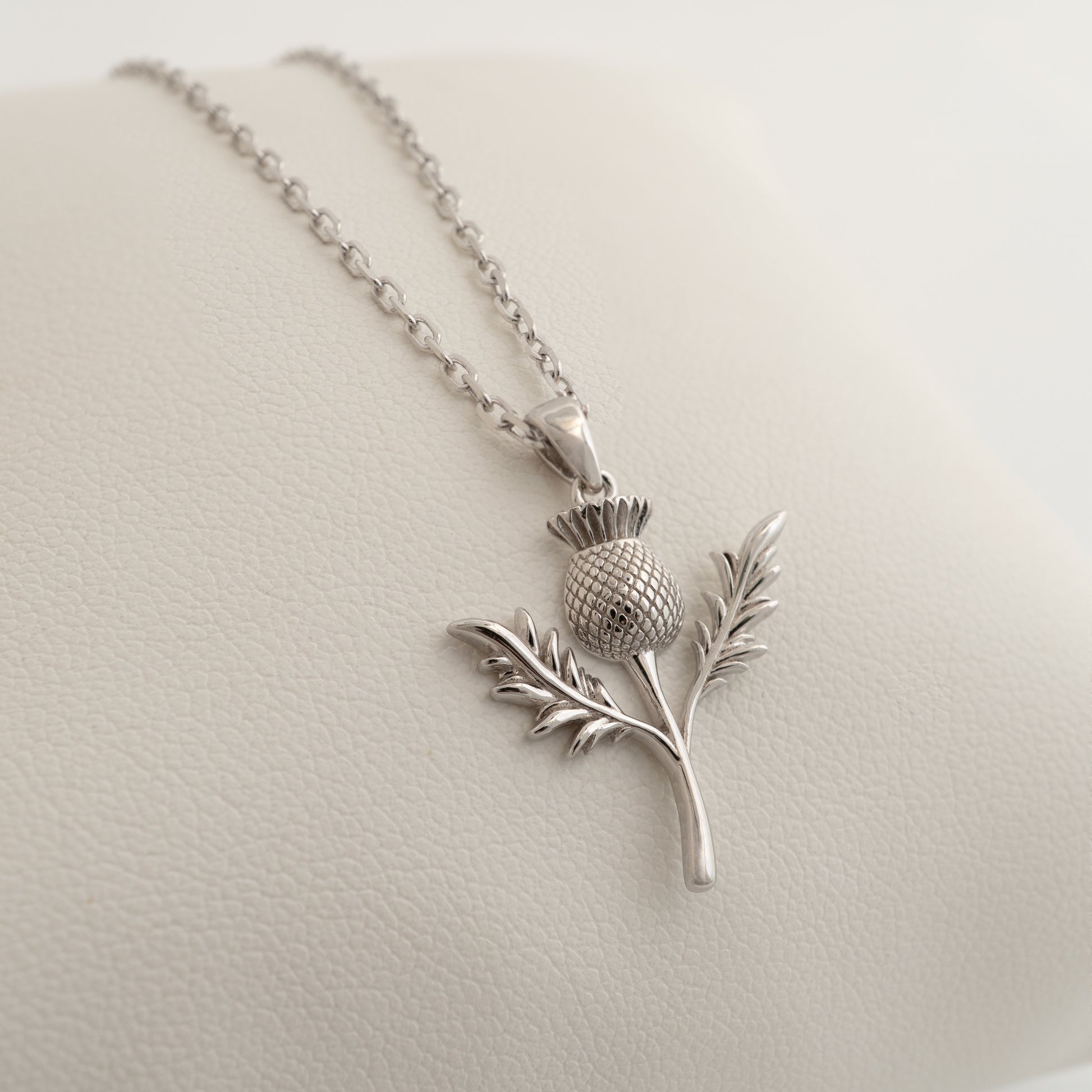 Silver thistle necklace pendant laid flat, showing leaf texture and chain