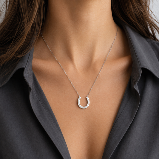 A close-up of a model wearing a delicate silver horseshoe pendant necklace with a textured, pavé-set appearance, styled with a dark gray button-down shirt.