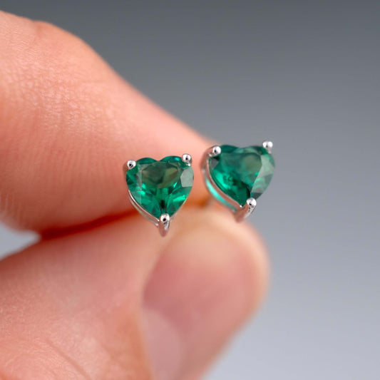 Close-up of lab emerald heart earrings held in fingers