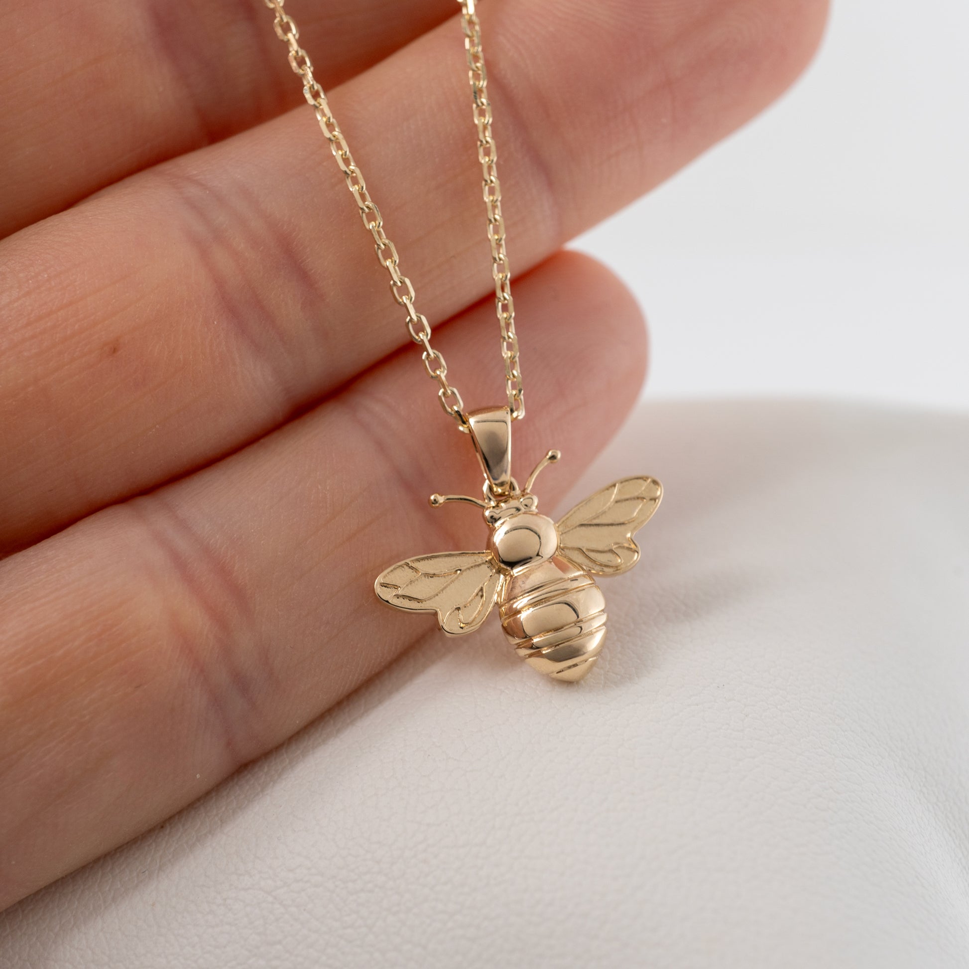 Solid gold bee necklace pendant shown in hand for scale, featuring curved antennae and an adjustable 9ct gold chain.