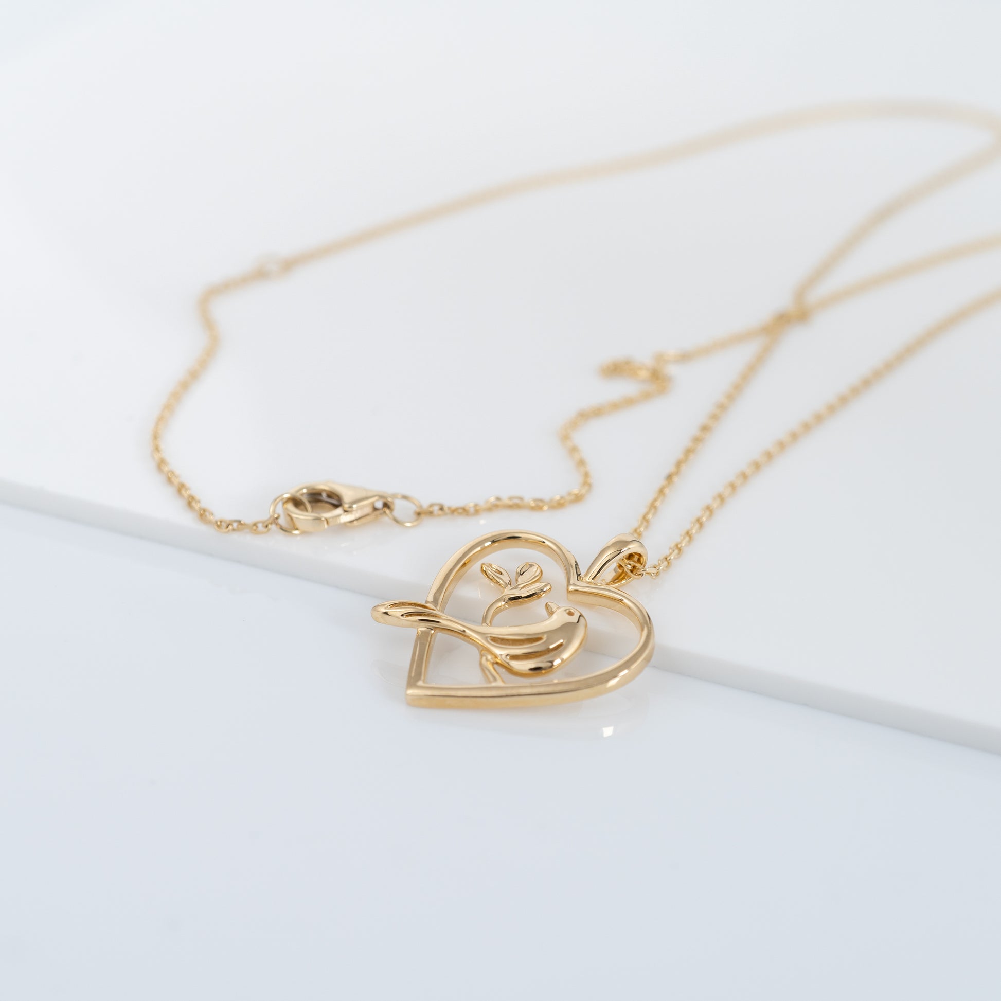 Flat lay of gold bird pendant with heart design