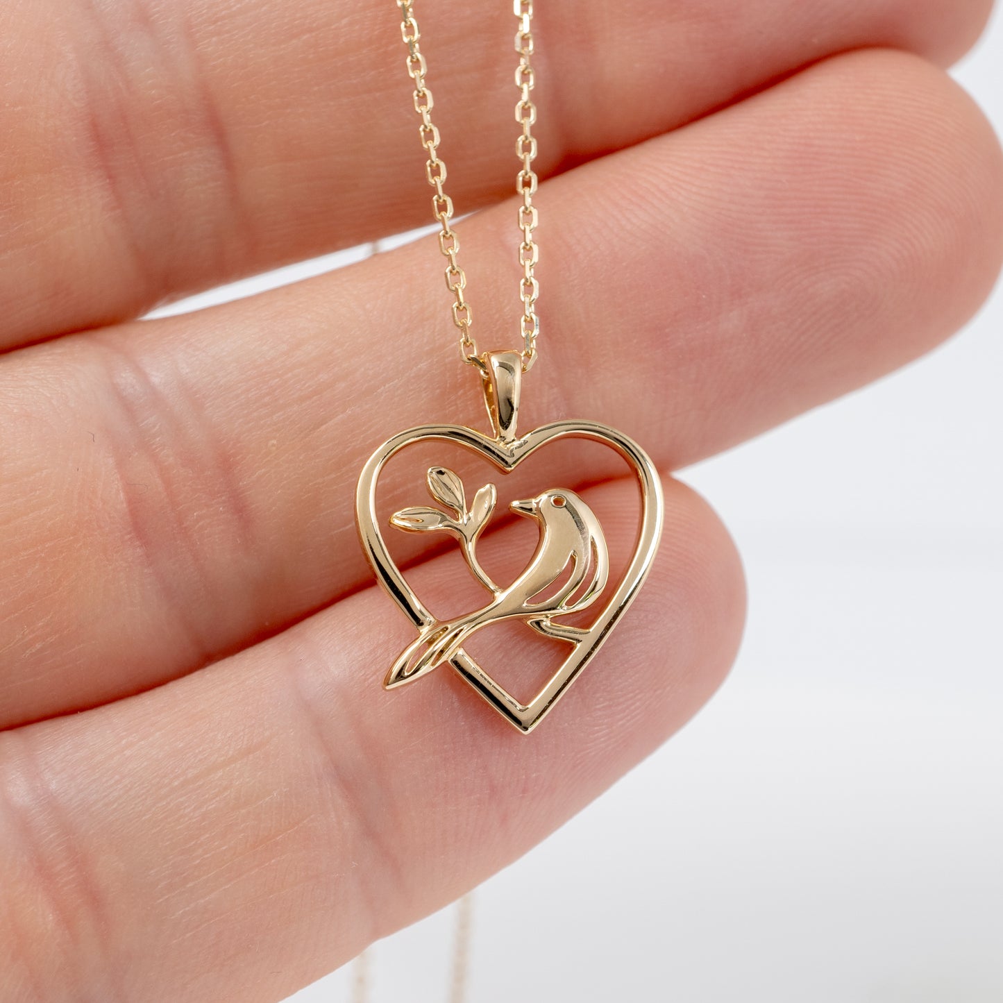 Close-up of gold bird heart pendant held in hand