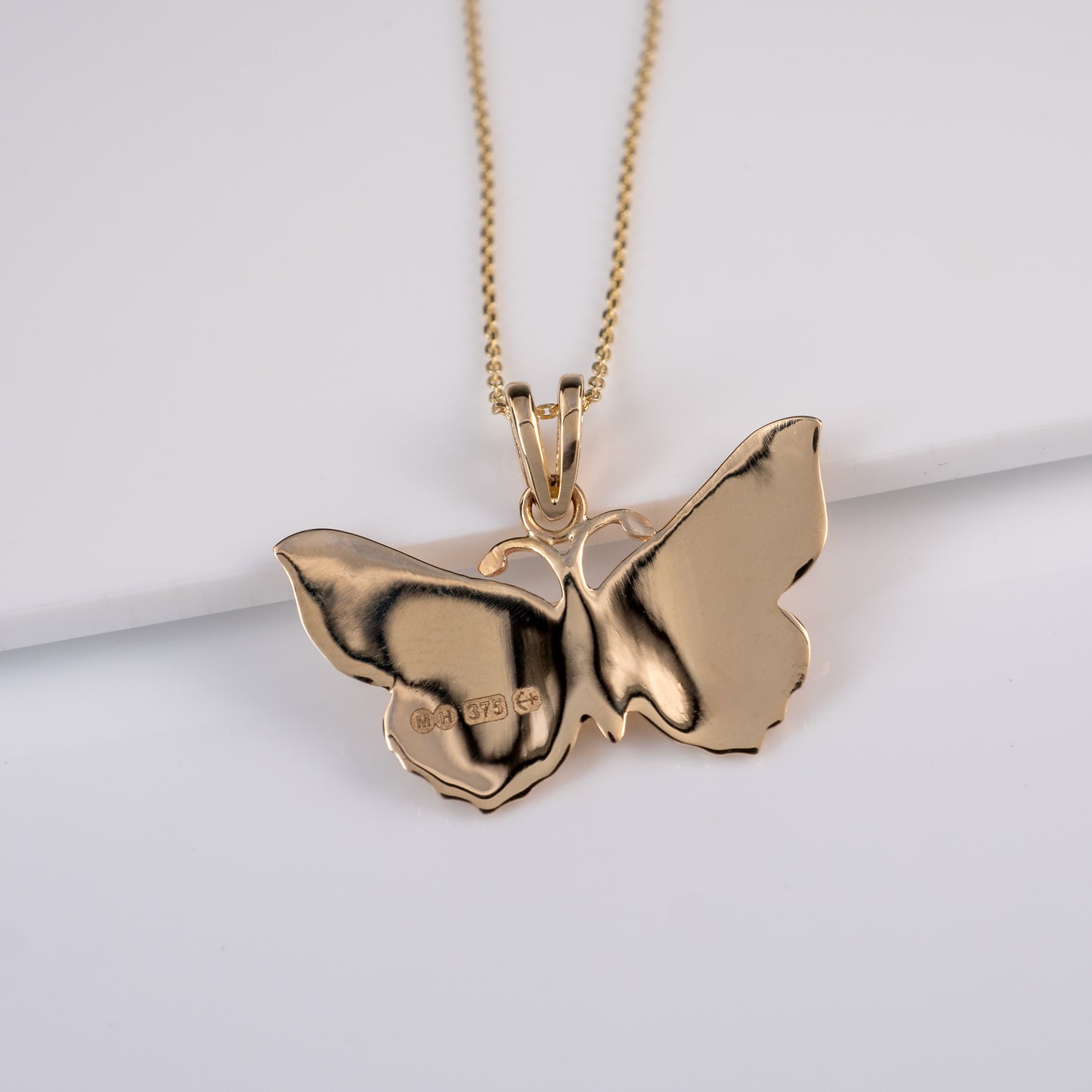 Back of gold butterfly pendant showing smooth polished finish and British assay hallmark