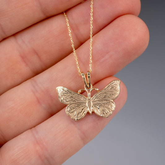 Gold butterfly pendant held in hand – close-up view