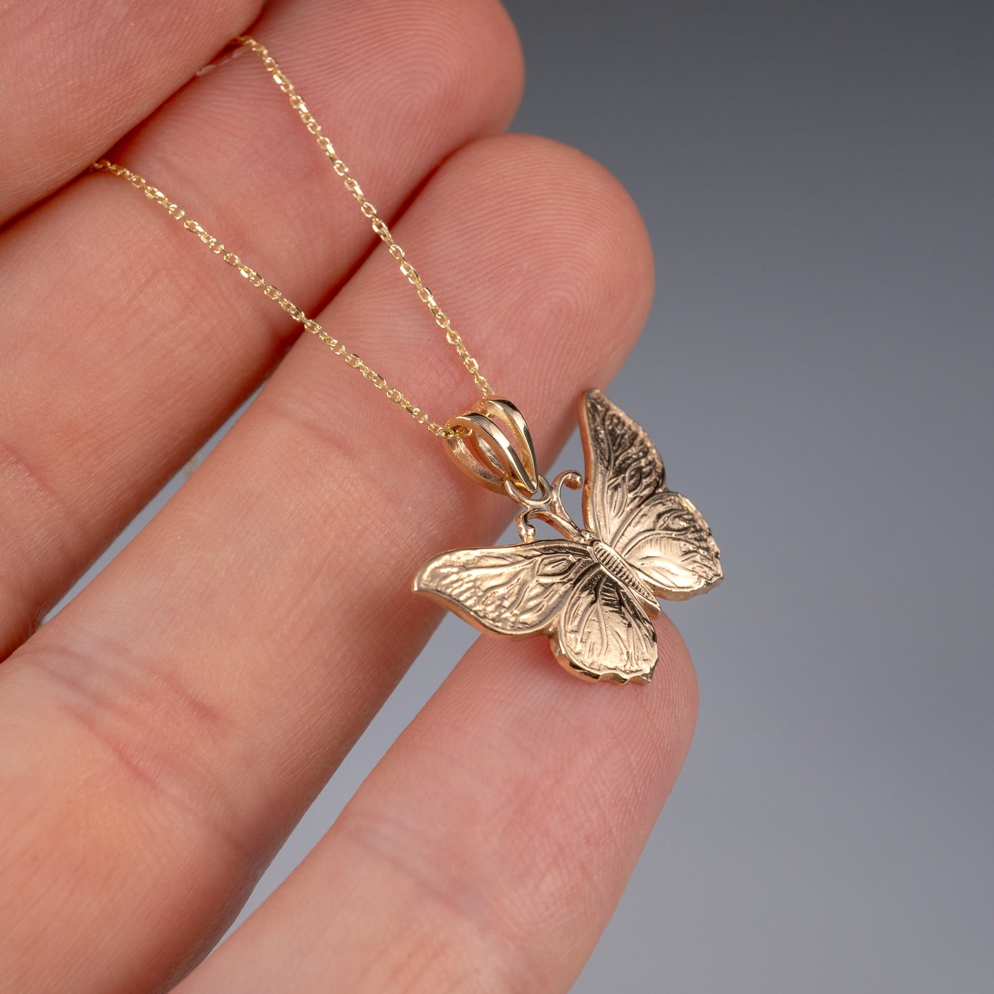 Side view of gold butterfly pendant held in hand
