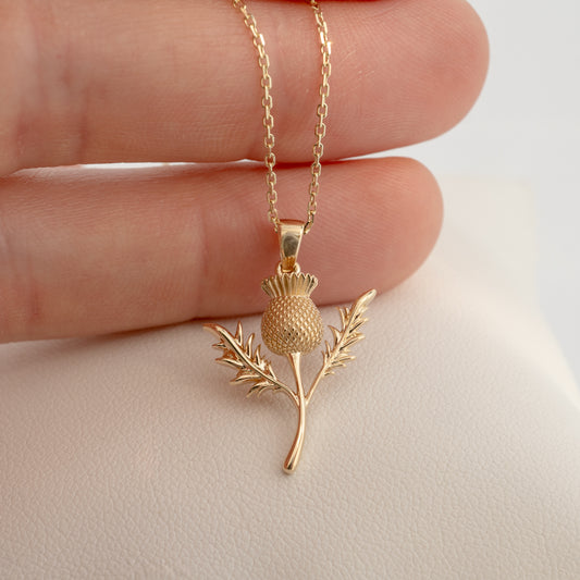Gold thistle pendant held in hand for scale reference