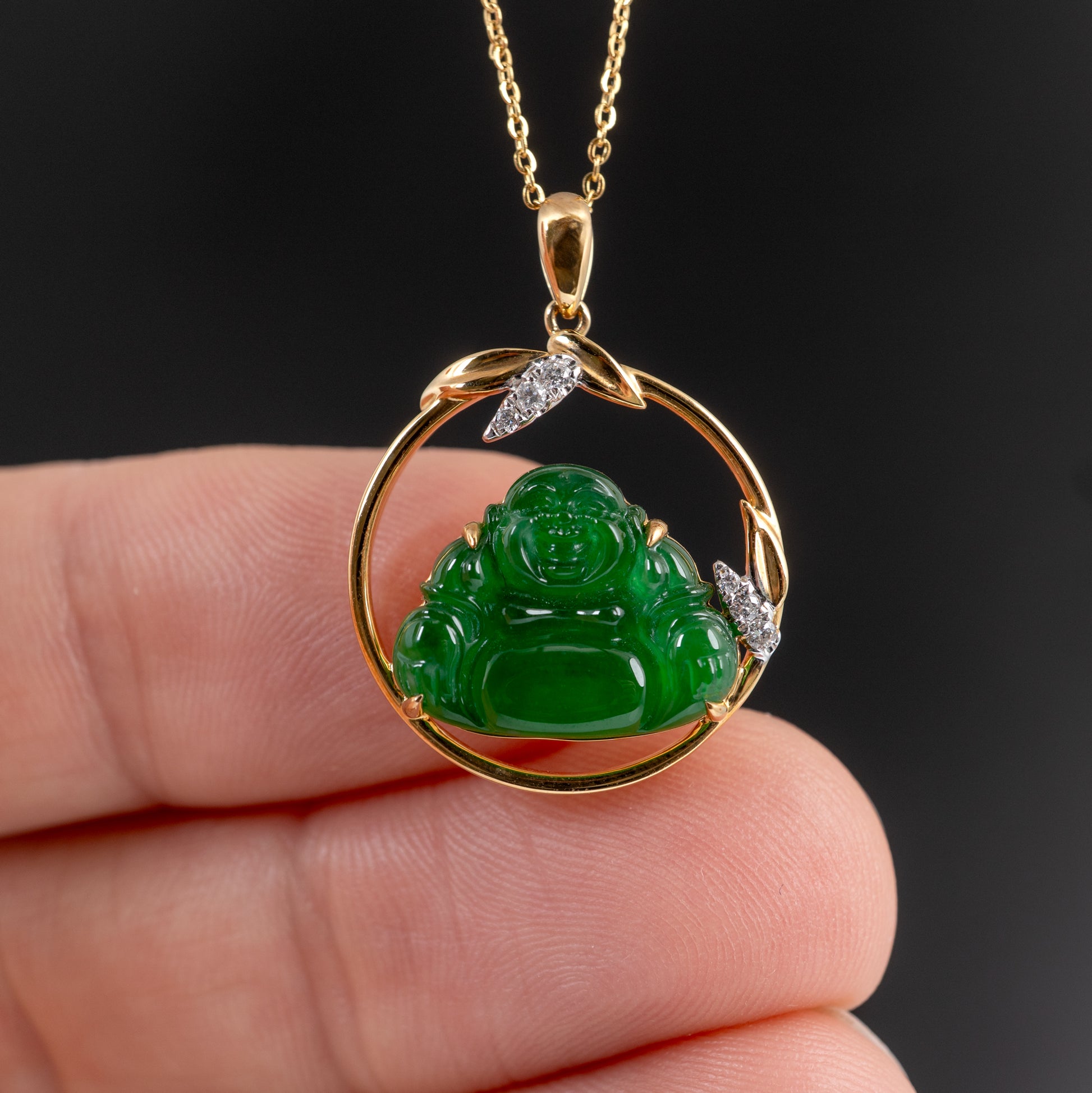 grade A Green jadeite Buddha pendant with gold frame held by a hand against a dark background