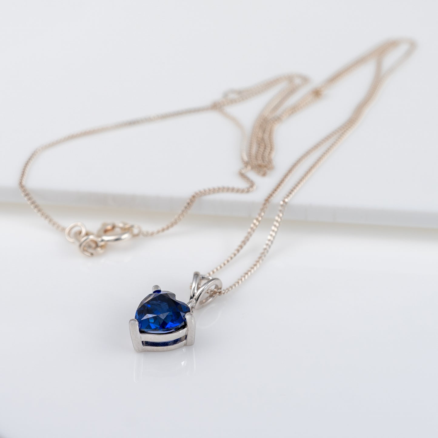 Heart-shaped lab sapphire pendant necklace laid out with adjustable silver chain