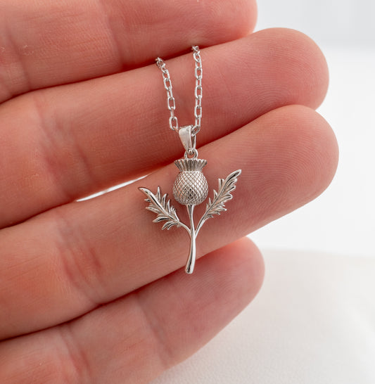 Sterling silver thistle pendant held in hand for size scale