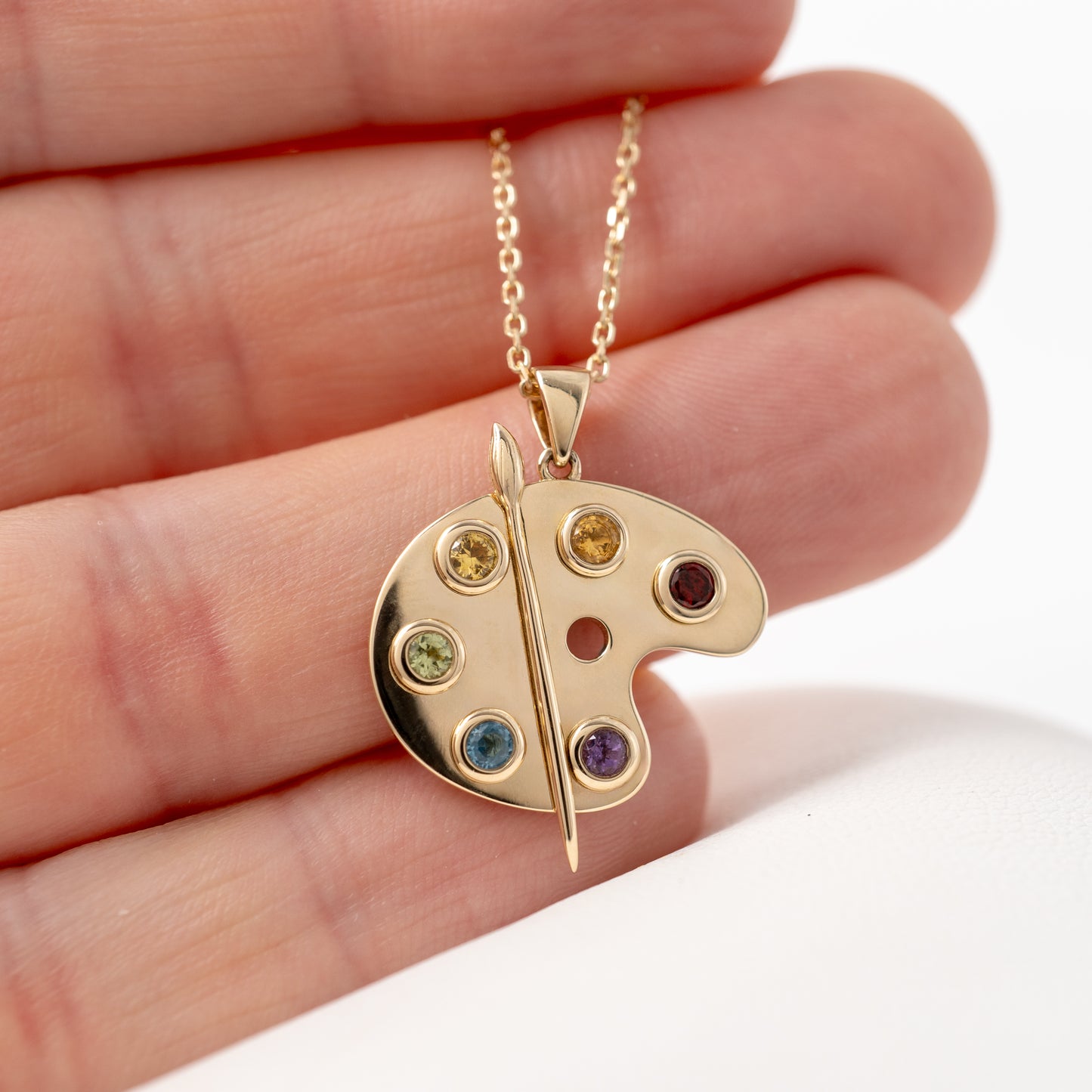 Gold artist palette pendant displayed in hand for size reference