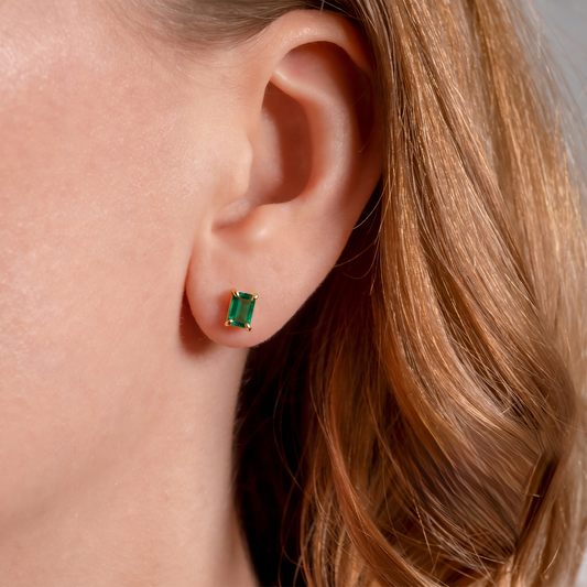 Rich green lab emerald rectangle stud earring in yellow gold-plated silver worn on the ear