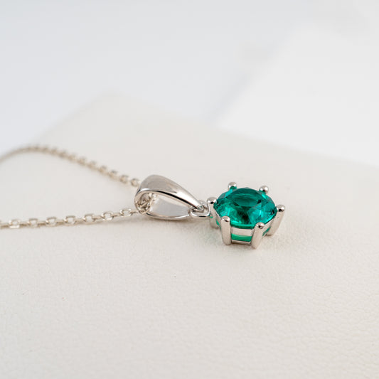lab grown emerald necklace in a silver prong setting, resting on a textured white surface.