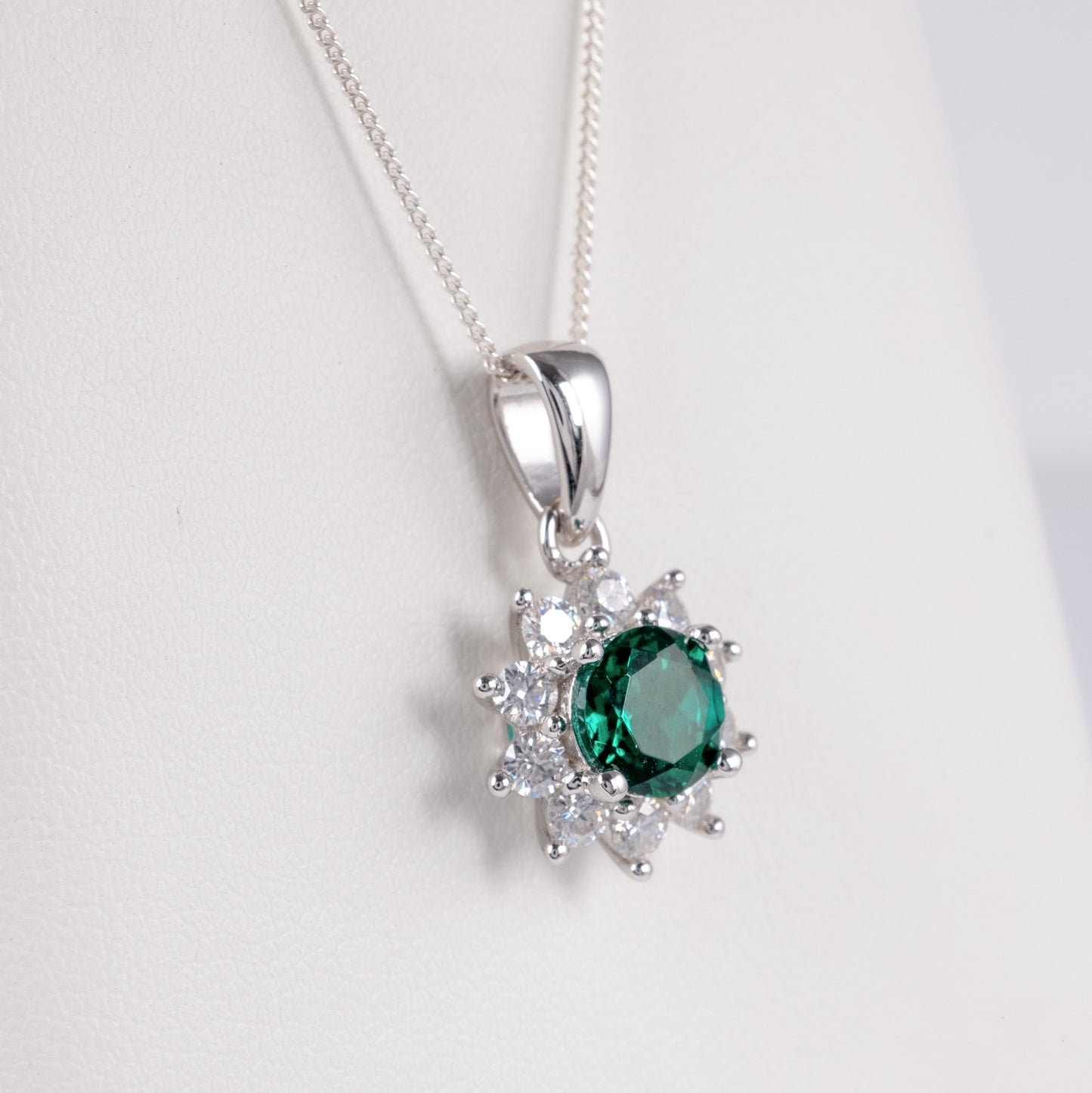 Close-up of lab grown emerald halo necklace in 925 silver on white background