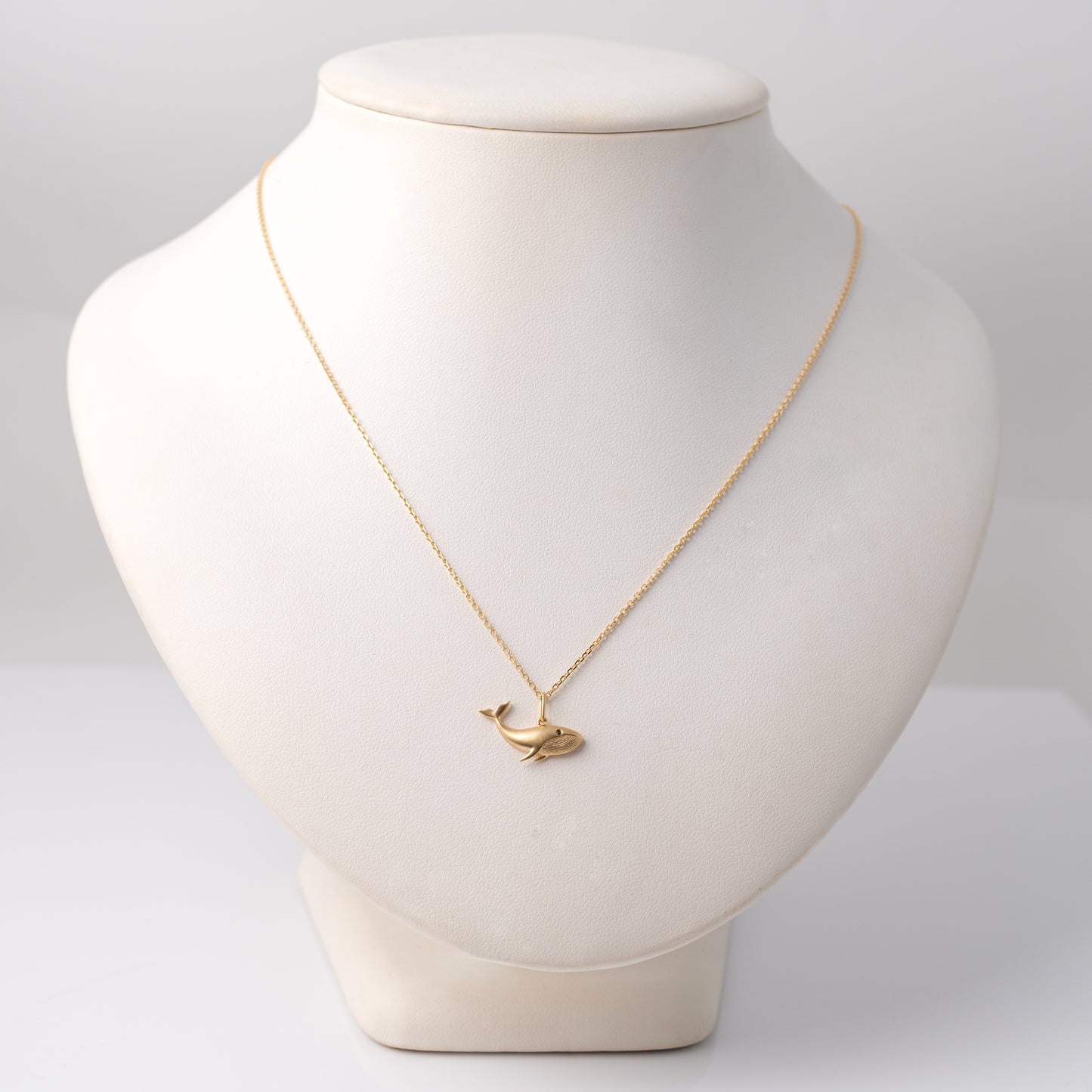 Matte gold whale pendant on a display bust to show scale