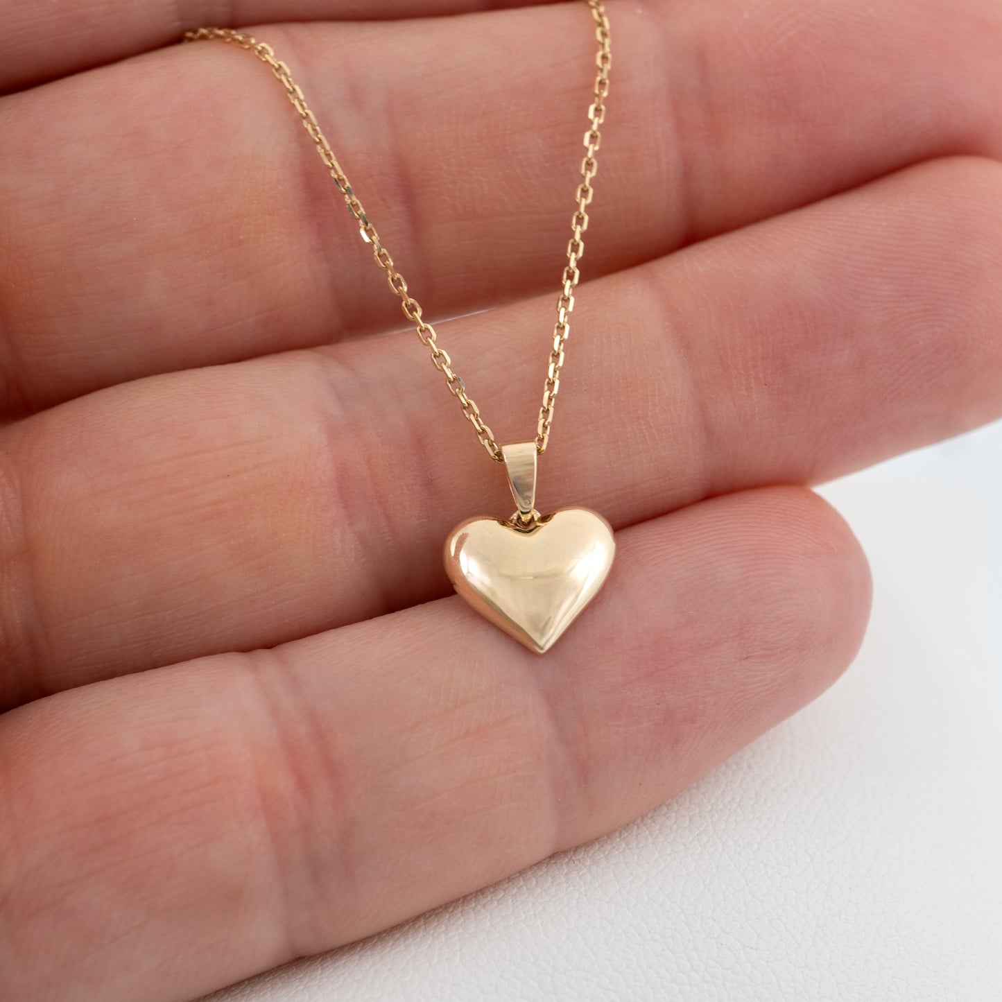 Small gold heart pendant necklace shown in hand for scale