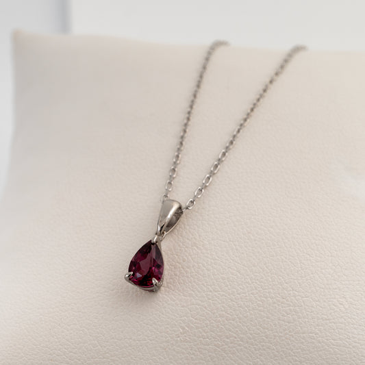Pear-cut rhodolite garnet pendant in sterling silver with a silver chain, resting on a white cushion.