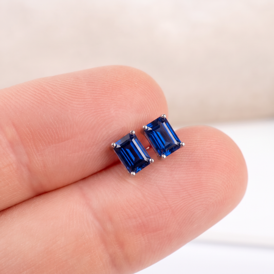 Pair of royal blue lab sapphire rectangle studs held between fingers to show size and colour