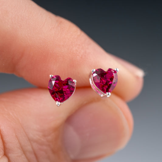 Ruby heart stud earrings held between fingers