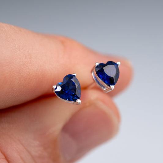 Pair of sapphire heart stud earrings shown in hand for scale