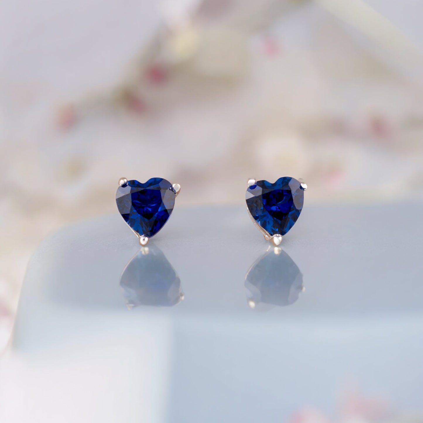 Sapphire heart earrings resting on light surface – 925 silver detail