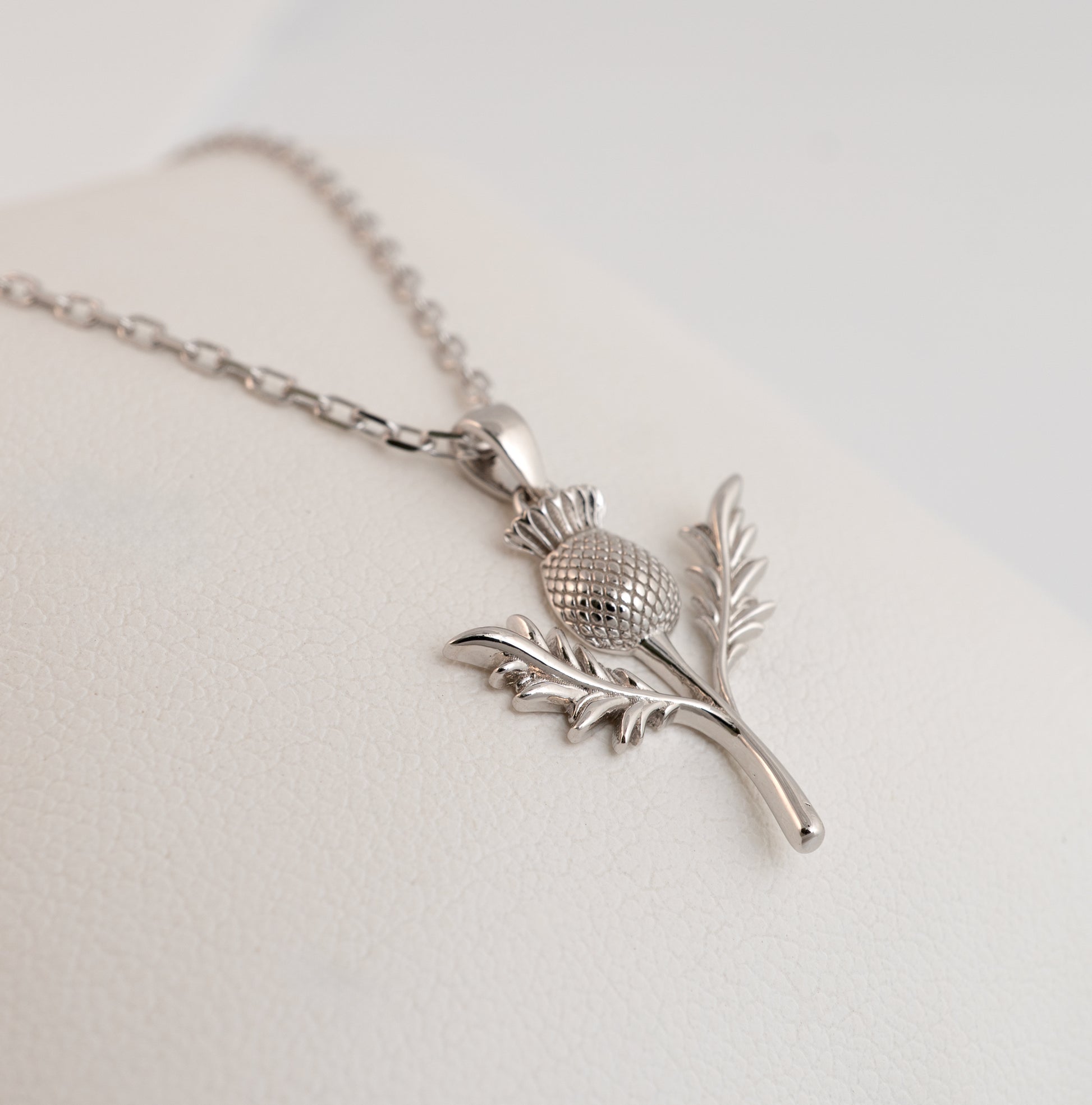 Close-up of thistle pendant detailing in silver on white