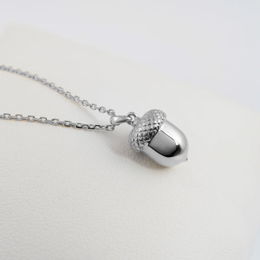 Sterling silver acorn pendant laid on white fabric with chain visible