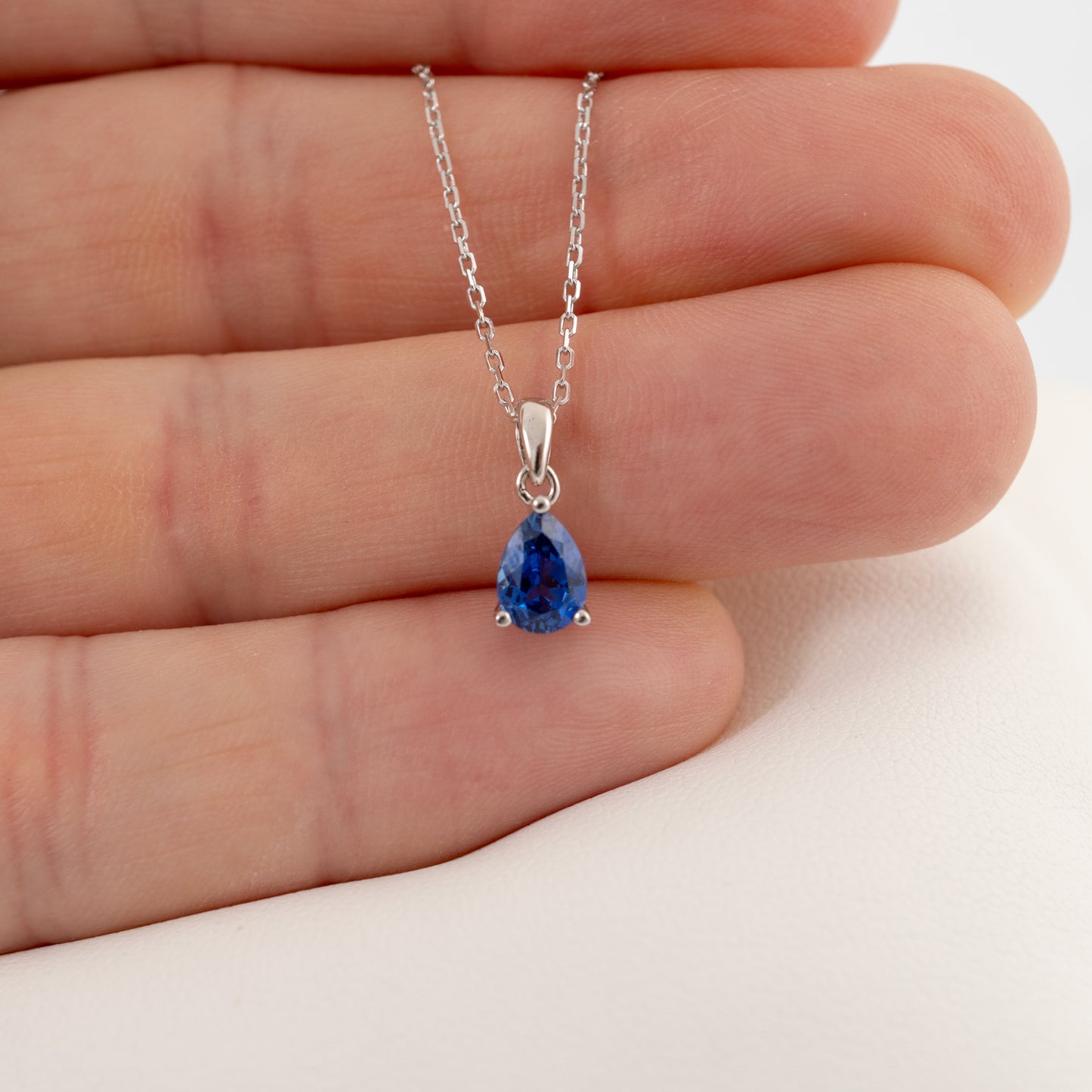 Sapphire teardrop necklace in silver shown in hand for scale