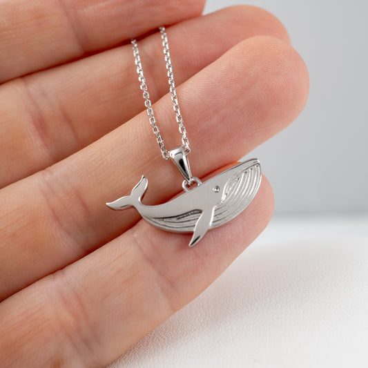 Silver whale necklace shown in hand for scale