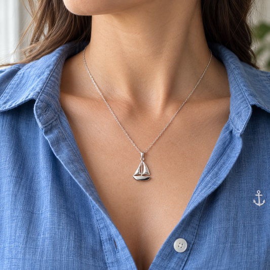 Model wearing a sterling silver sailing boat necklace with an open blue shirt