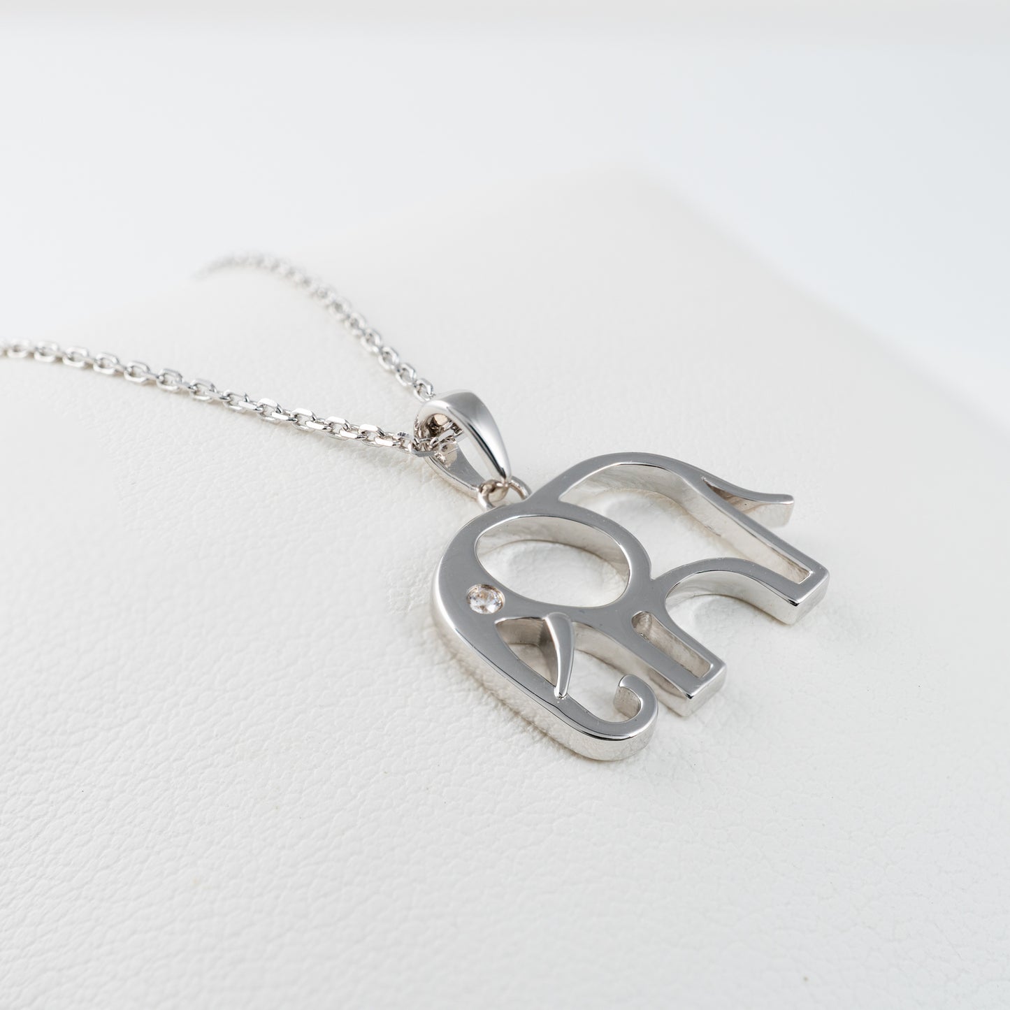 Polished silver elephant pendant necklace laid flat on white leather