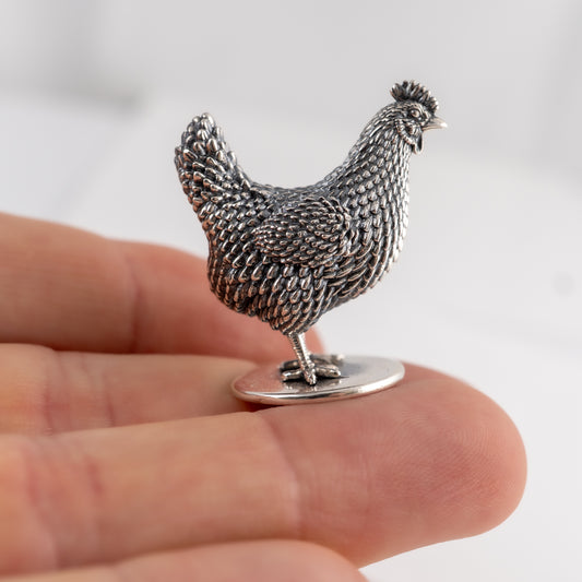 Silver chicken figurine held in a hand against a light background